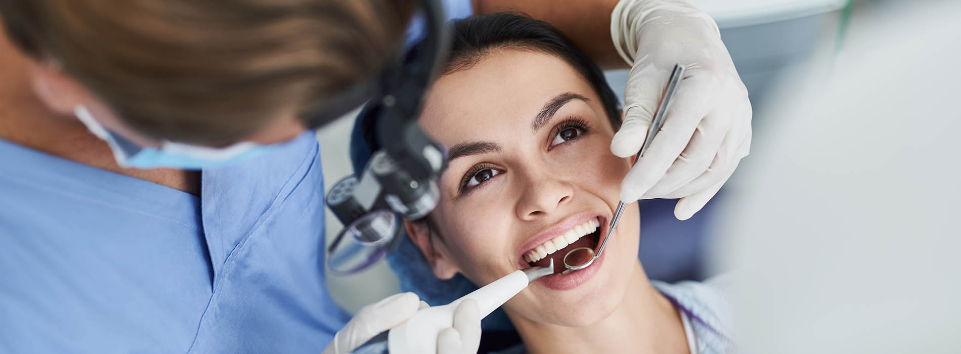 A woman receiving dental care from a dentist with other medical professionals assisting.