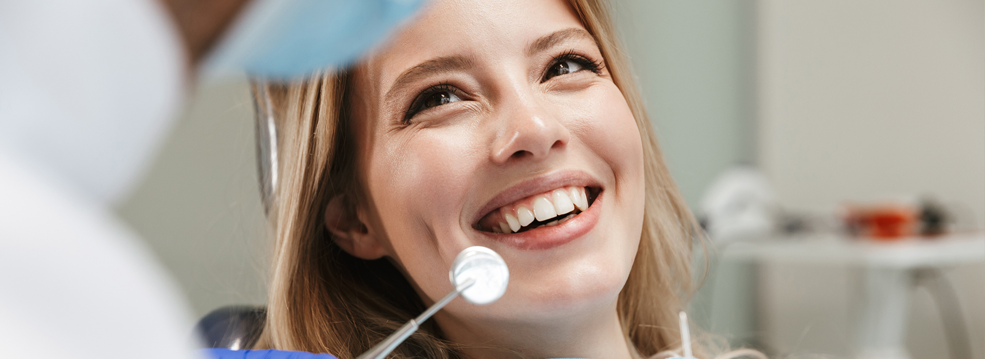 A woman in a dental chair with a dentist holding a mirror, smiling at her reflection.
