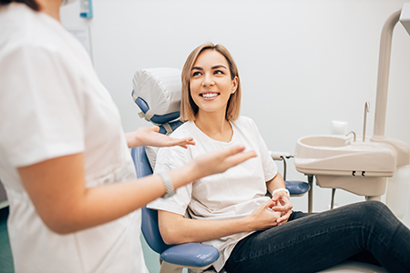 A woman sitting in a dental chair with a smile on her face while being attended to by a dentist and dental hygienist.